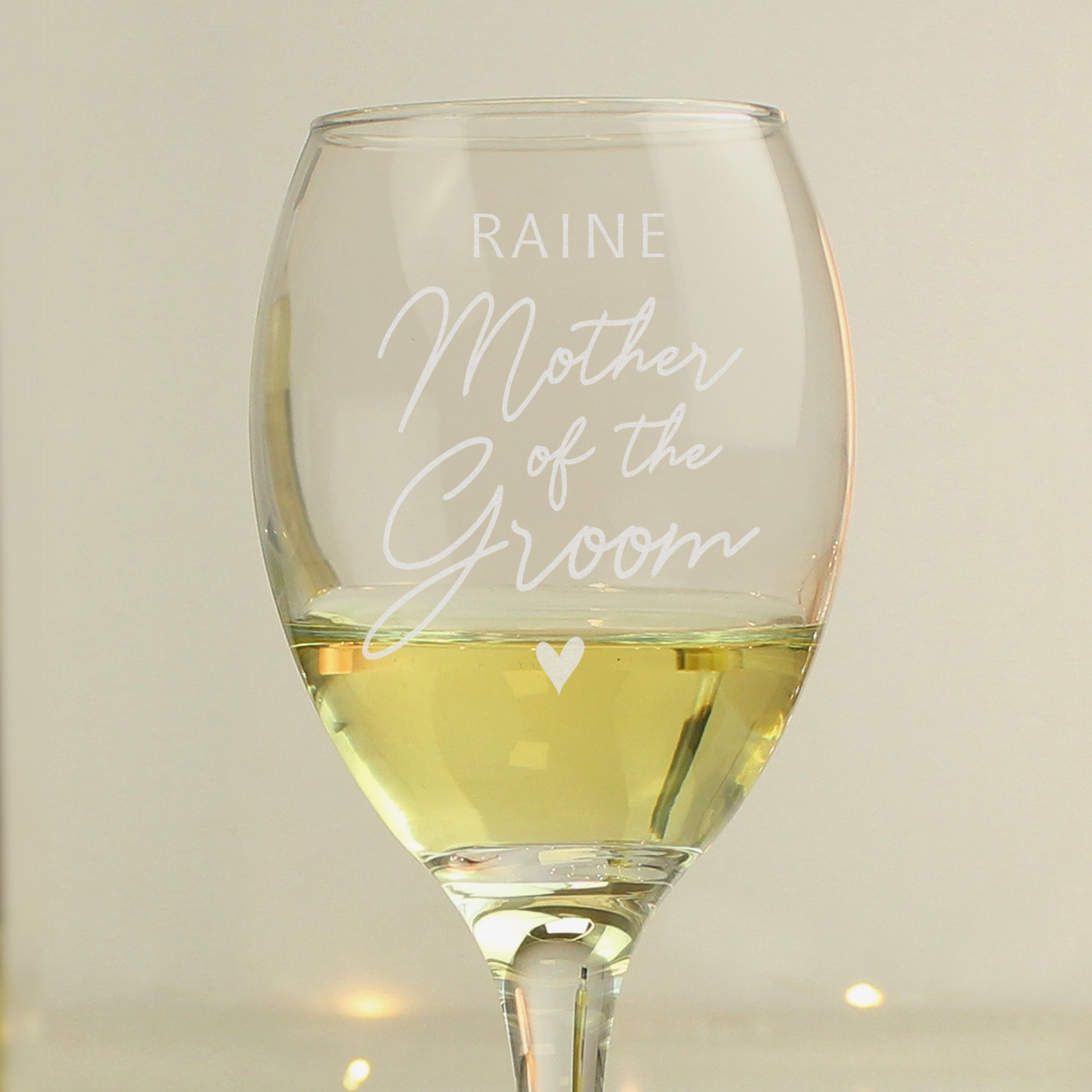 Wine glass with 'Raine Mother of the Groom' engraving filled with white wine on a neutral background