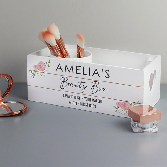 White wooden storage crate with pink rose design on the corners. Heart shaped cut out handles. Shown among perfume bottle and compact.