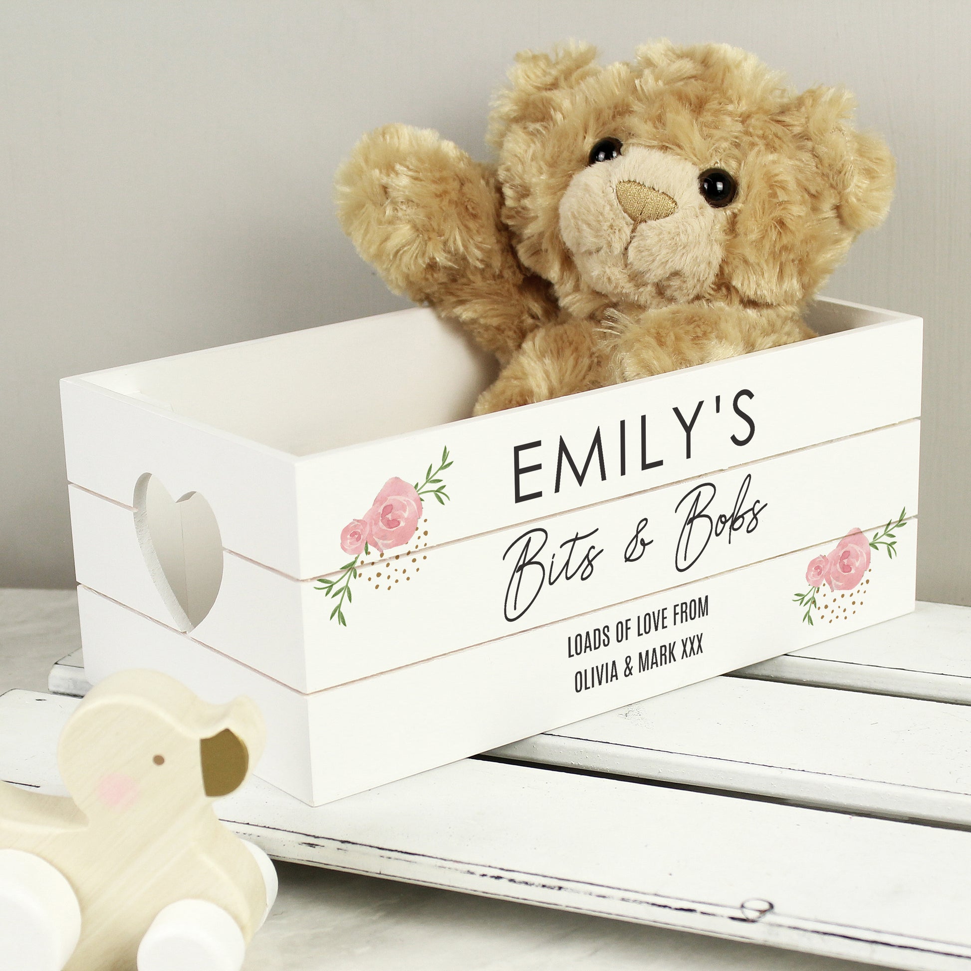 White wooden storage crate with pink rose design on the corners. Heart shaped cut out handles. Shown  with teddy.