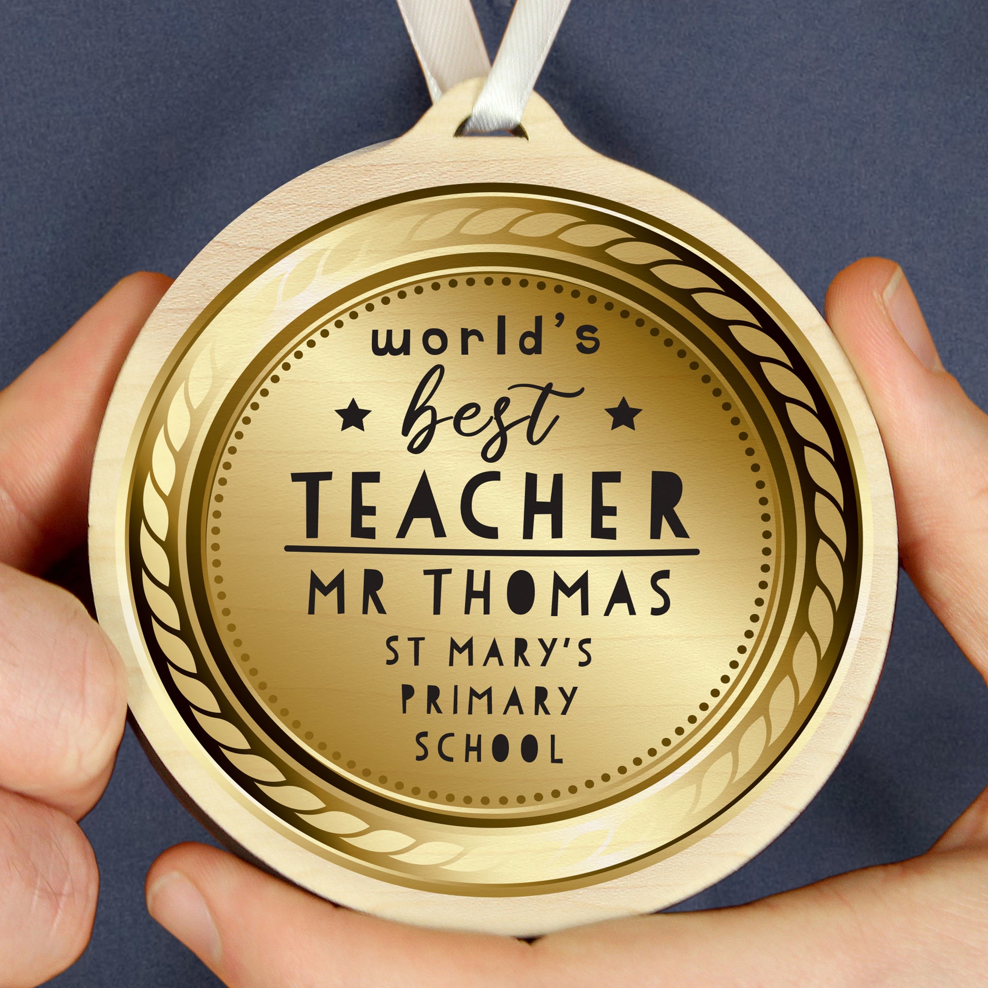 Gold coloured medal with 'World's Best Teacher' text held by hands against a dark background