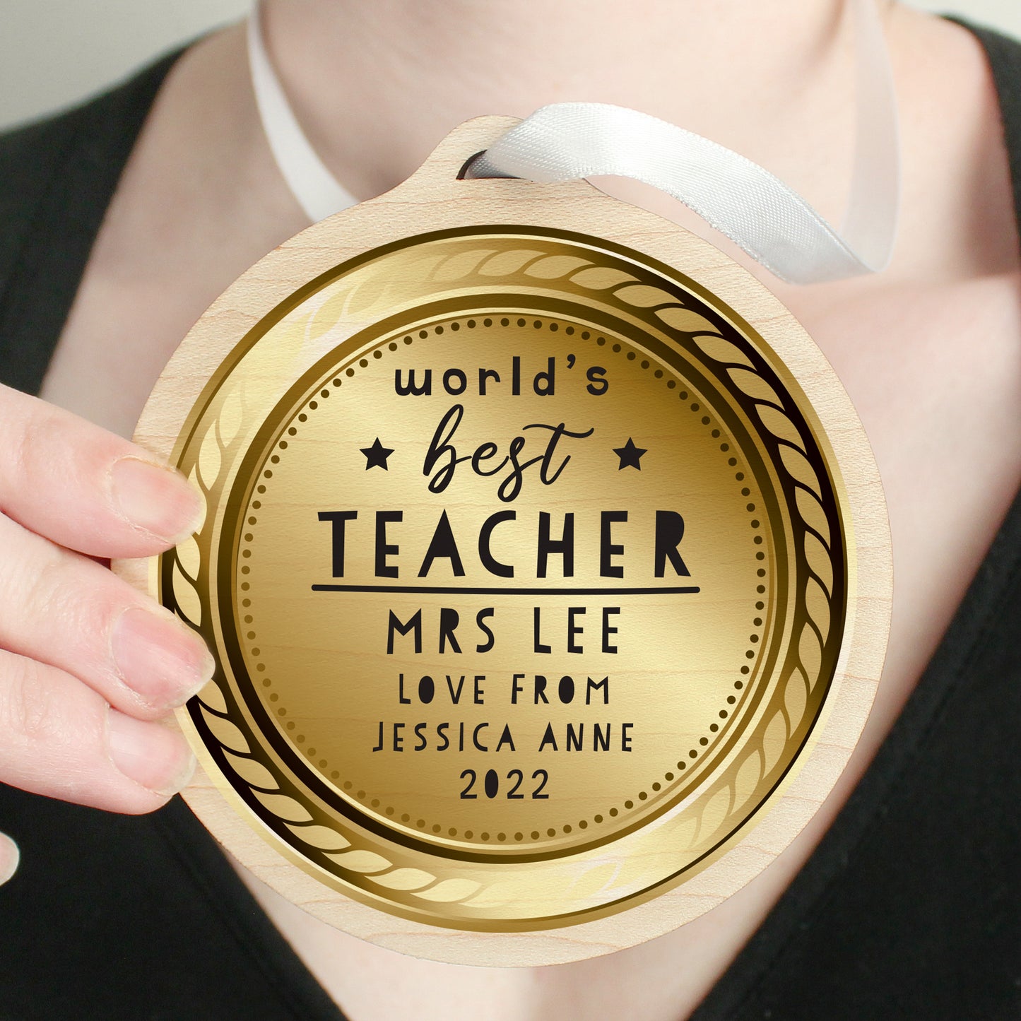 Gold coloured medal with 'World's Best Teacher' engraved, held by a person.