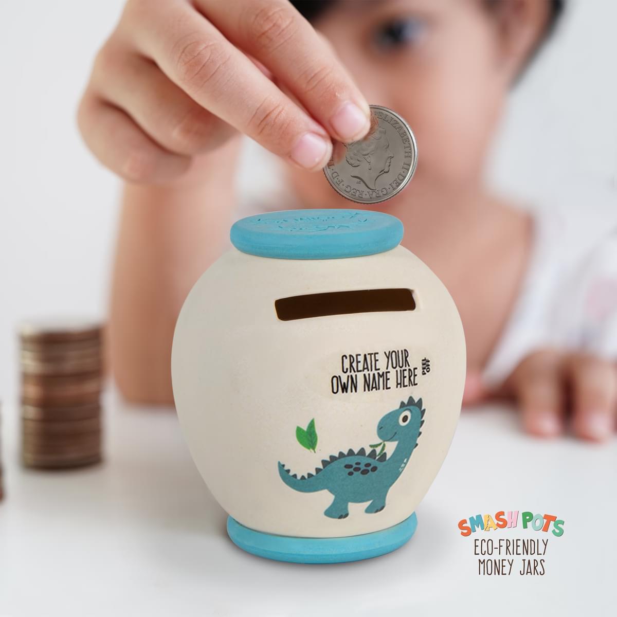 Small Smash Pot with Create Your Own Name sticker. Single use money saving jar. When full smash and bury in compost. Ivory with blue top and base. Colourful dinosaur image.