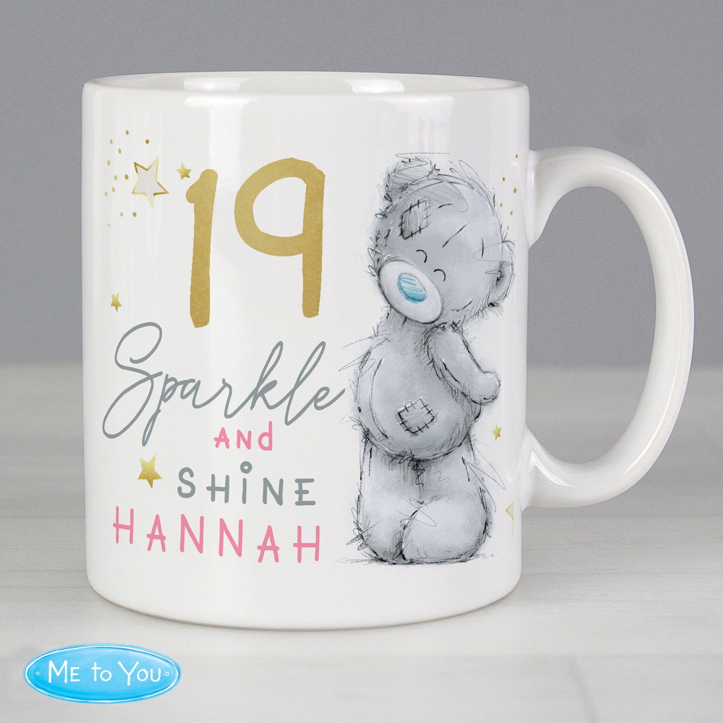 White mug with a bear illustration and text '19 Sparkle and Shine Hannah' on a gray background