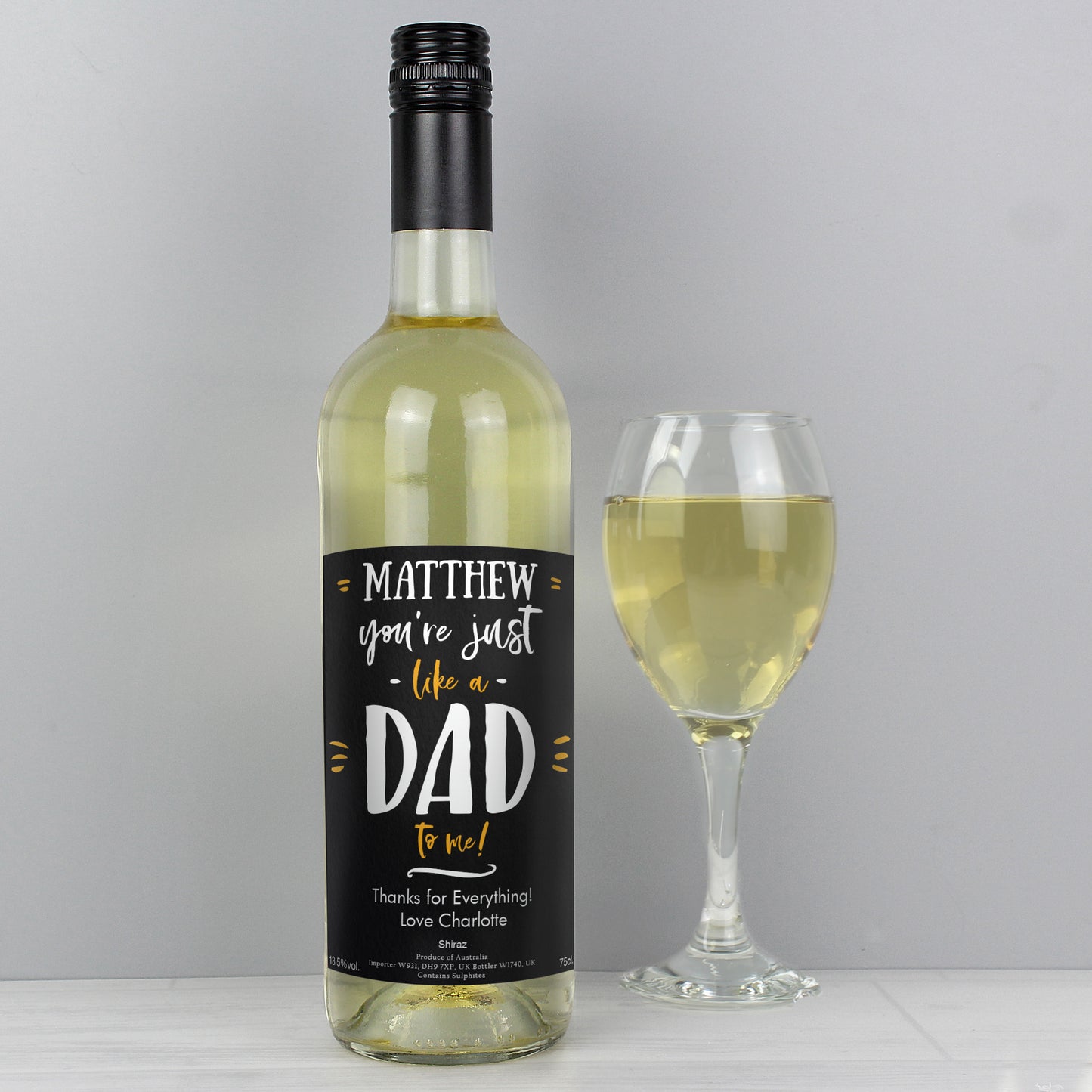 Wine bottle with a personalised label next to a glass of white wine on a grey background