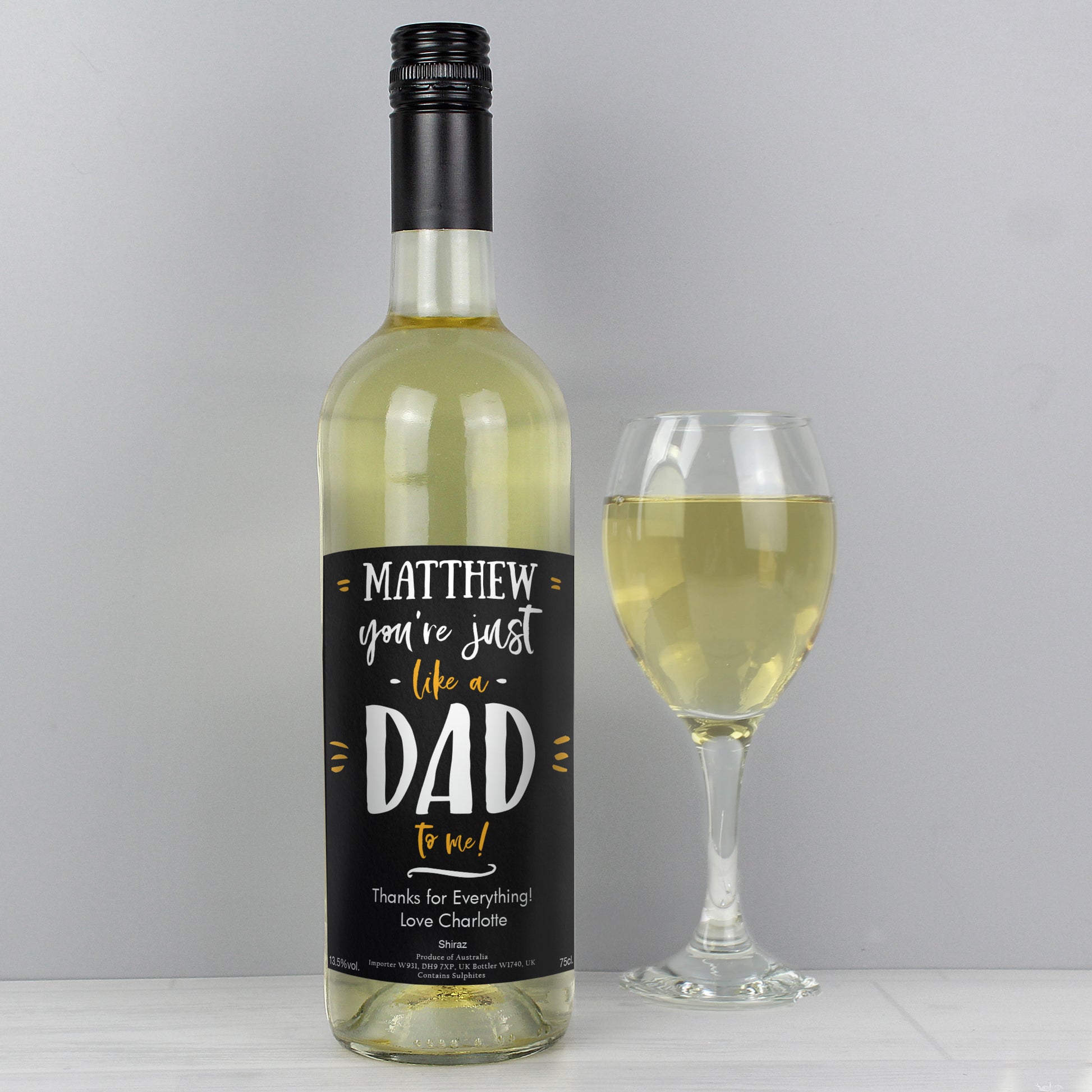 Wine bottle with a personalised label next to a glass of white wine on a grey background