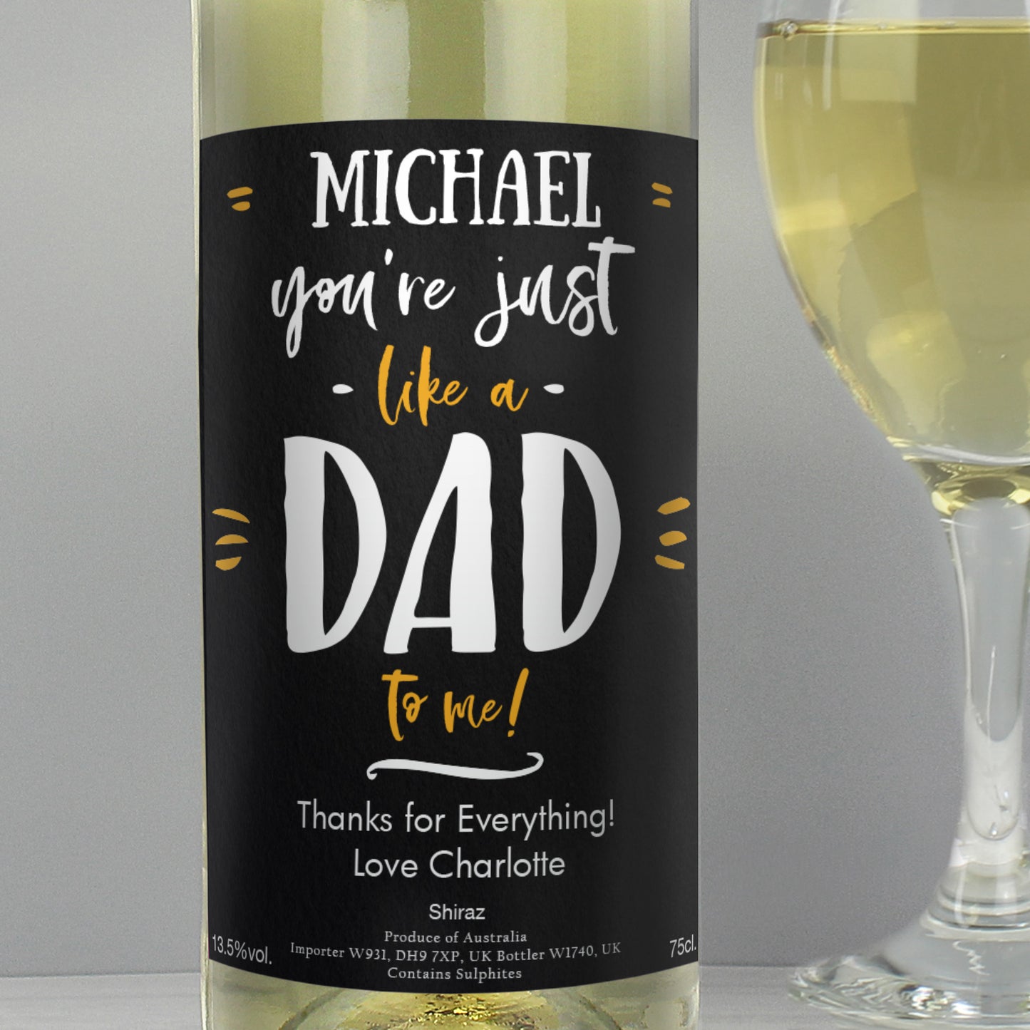 Wine bottle with a personalised label next to a glass of white wine on a grey background