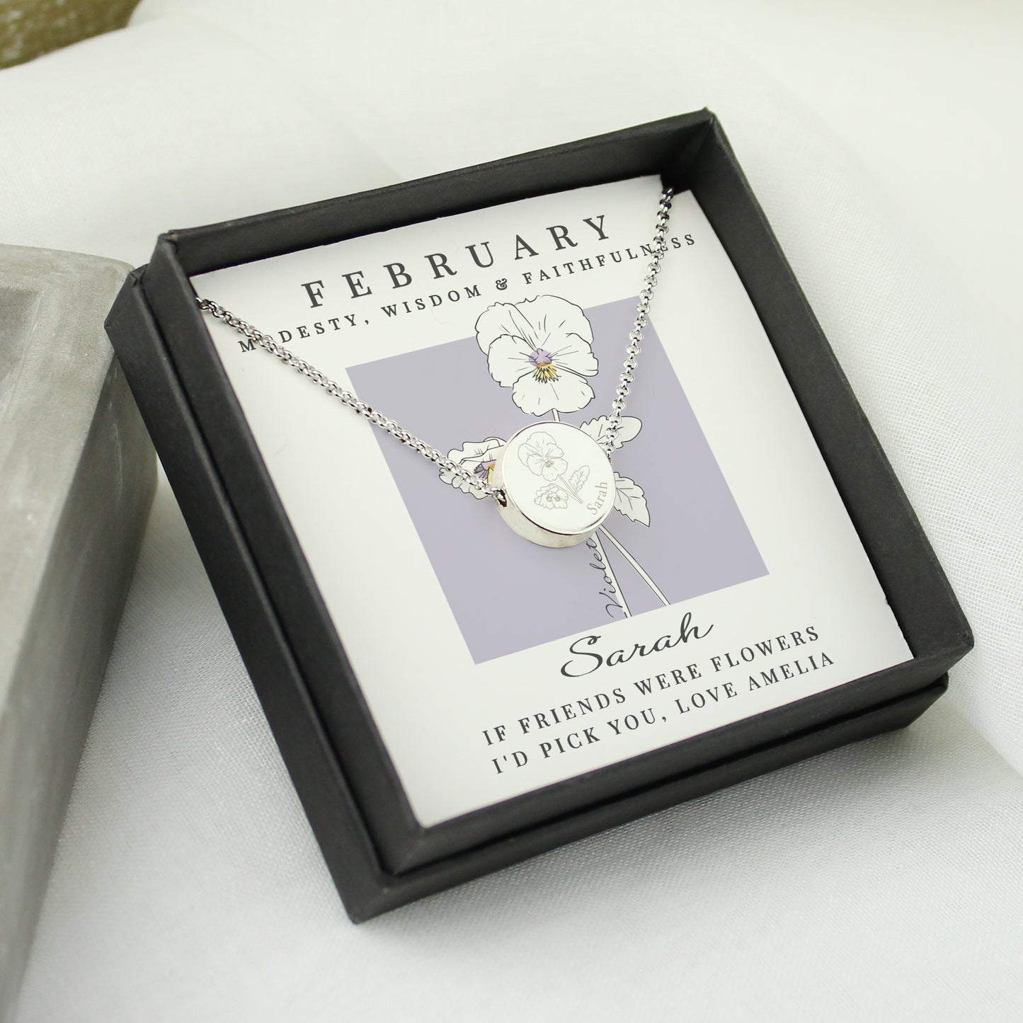 Silver necklace with a flower pendant in a black box on a white surface