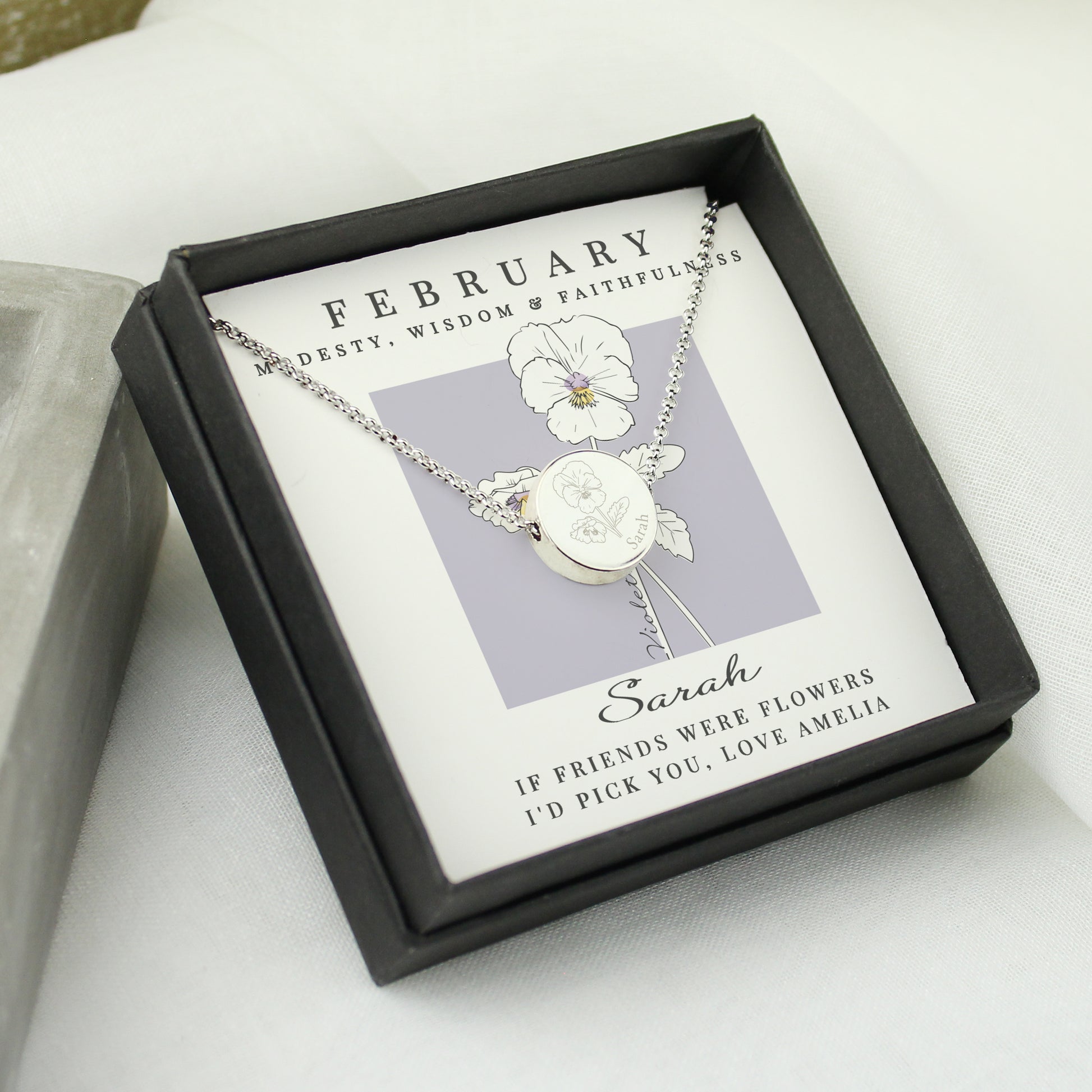Silver necklace with a flower pendant in a black box on a white surface