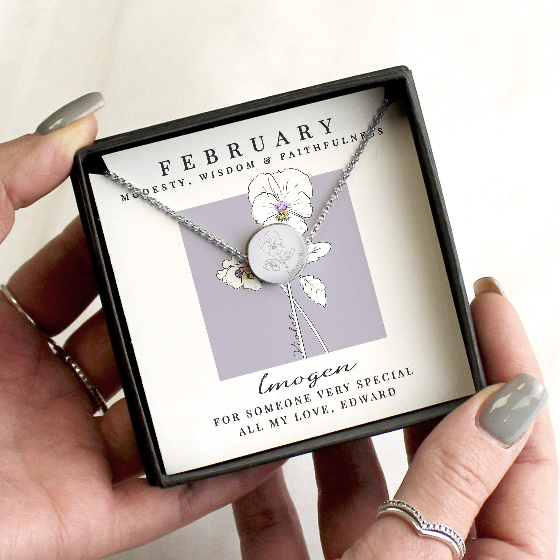 Necklace with February birth flower held by hands with manicured nails.