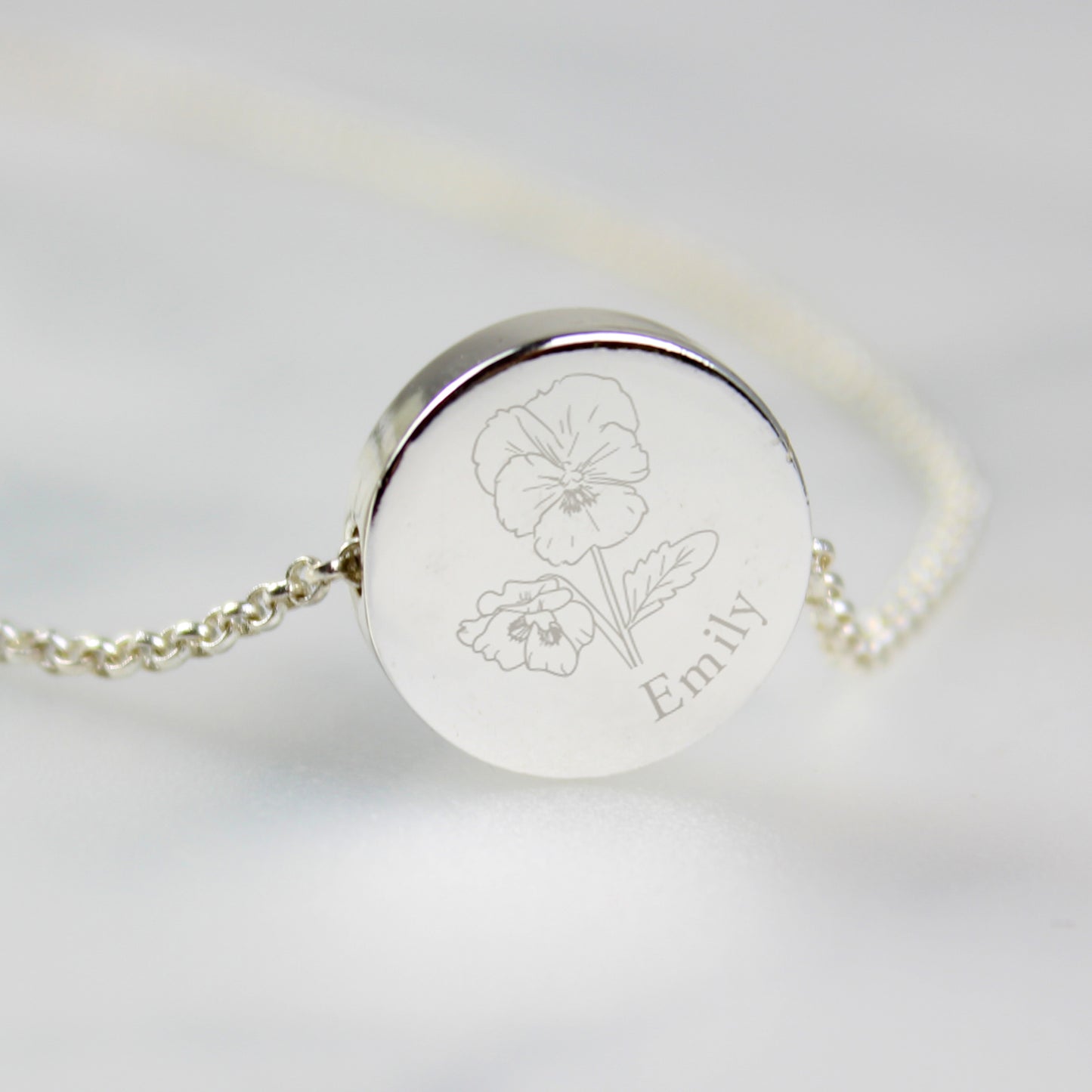 Silver coloured bracelet with engraved flower design and name 'Emily' on a light grey background
