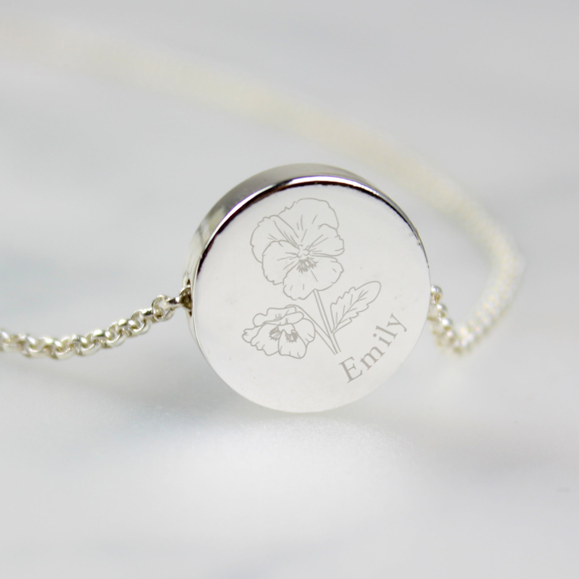 Silver coloured bracelet with engraved flower design and name 'Emily' on a light grey background