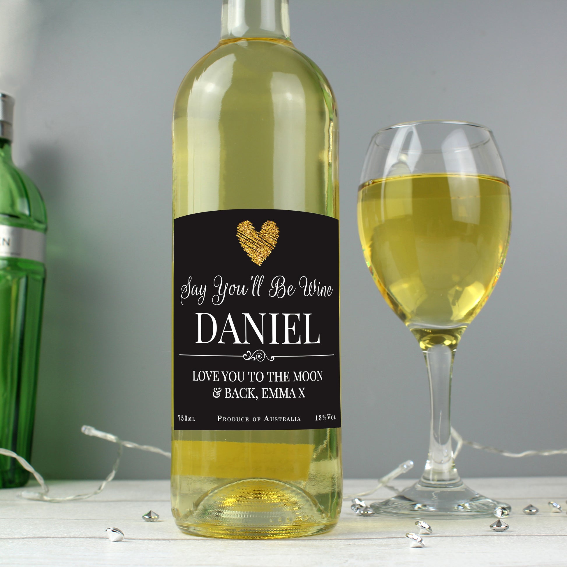 Wine bottle with a personalised label next to a glass of white wine on a grey background