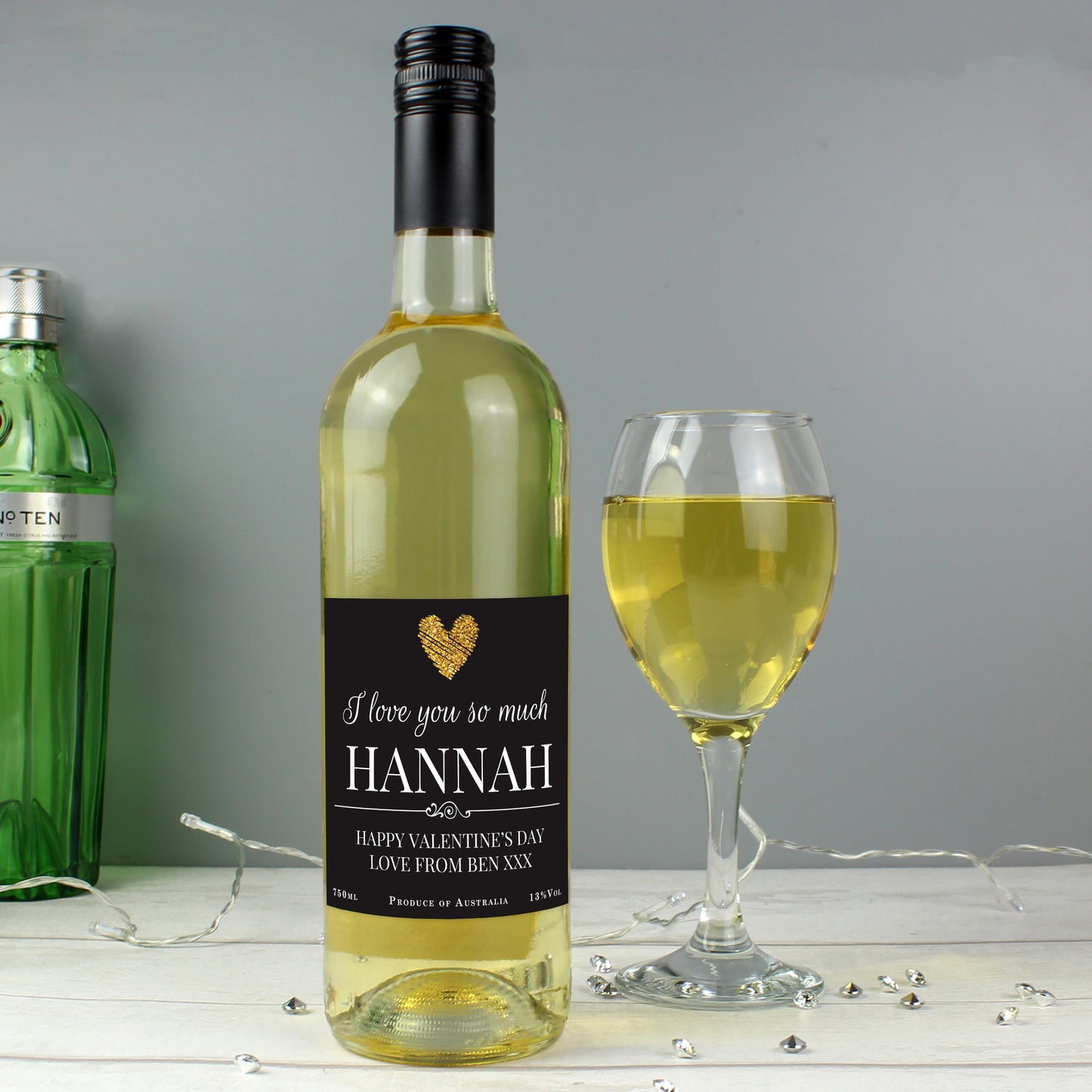 Bottle of white wine with a personalised label next to a glass of wine on a grey background